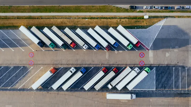 An aerial view of a freight yard with two rows of articulated lorry trailers parked in a herringbone pattern.