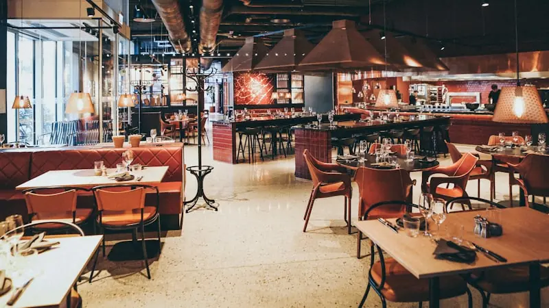 A wide restaurant interior with an open kitchen behind a counter, terracotta banquettes and copper extractor hoods.