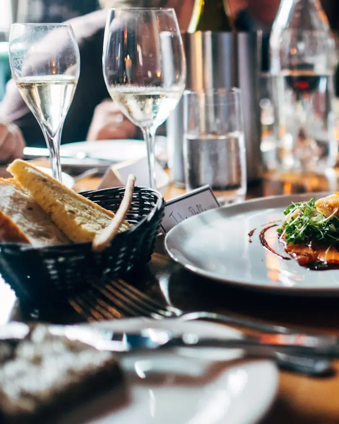 A restaurant table set for dinner, two glasses of sparkling wine behind a basket of bread and a plated salmon starter.
