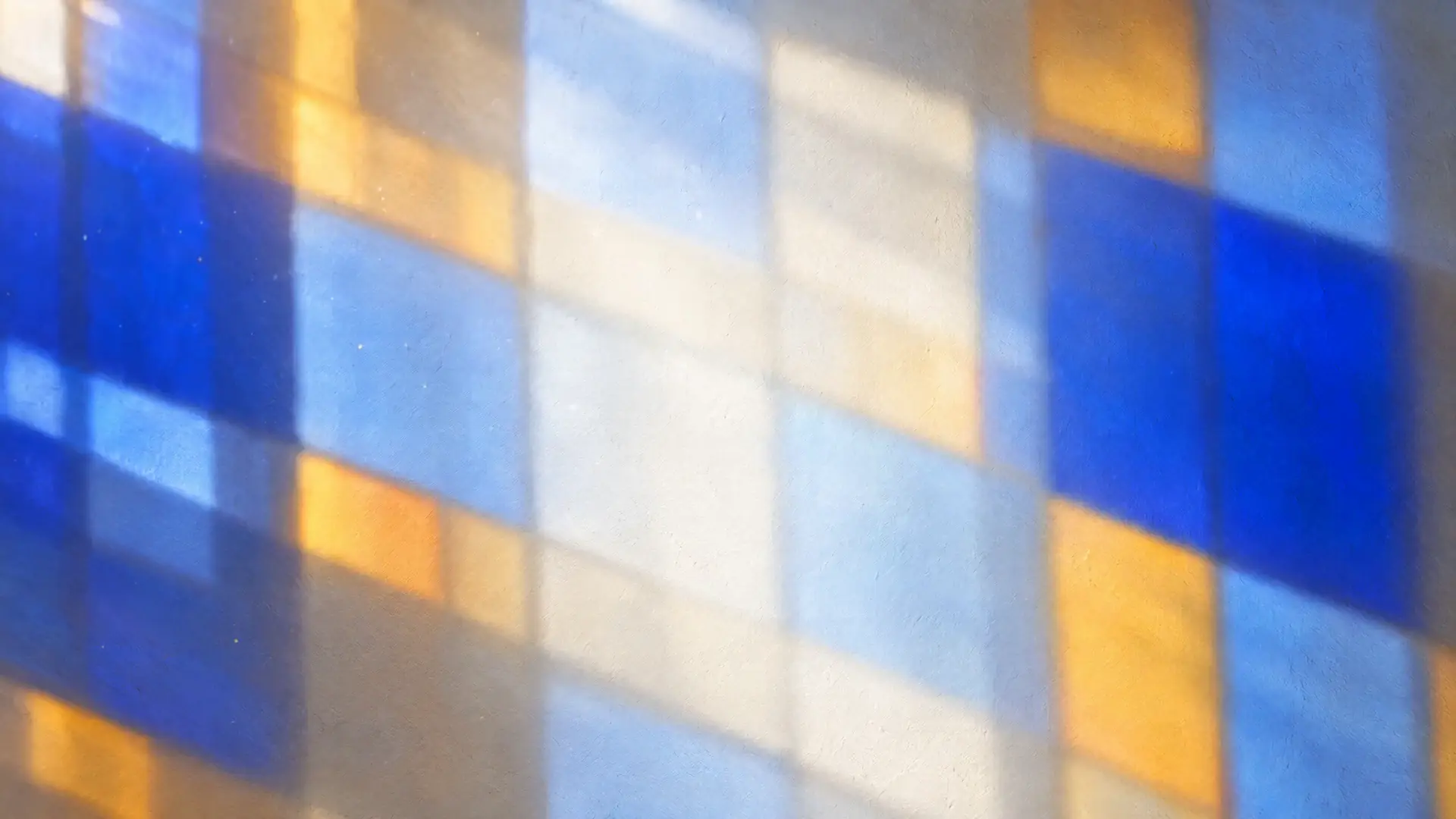 Sunlight through a stained-glass window casting a mosaic of Klein blue and amber light across a warm plaster wall