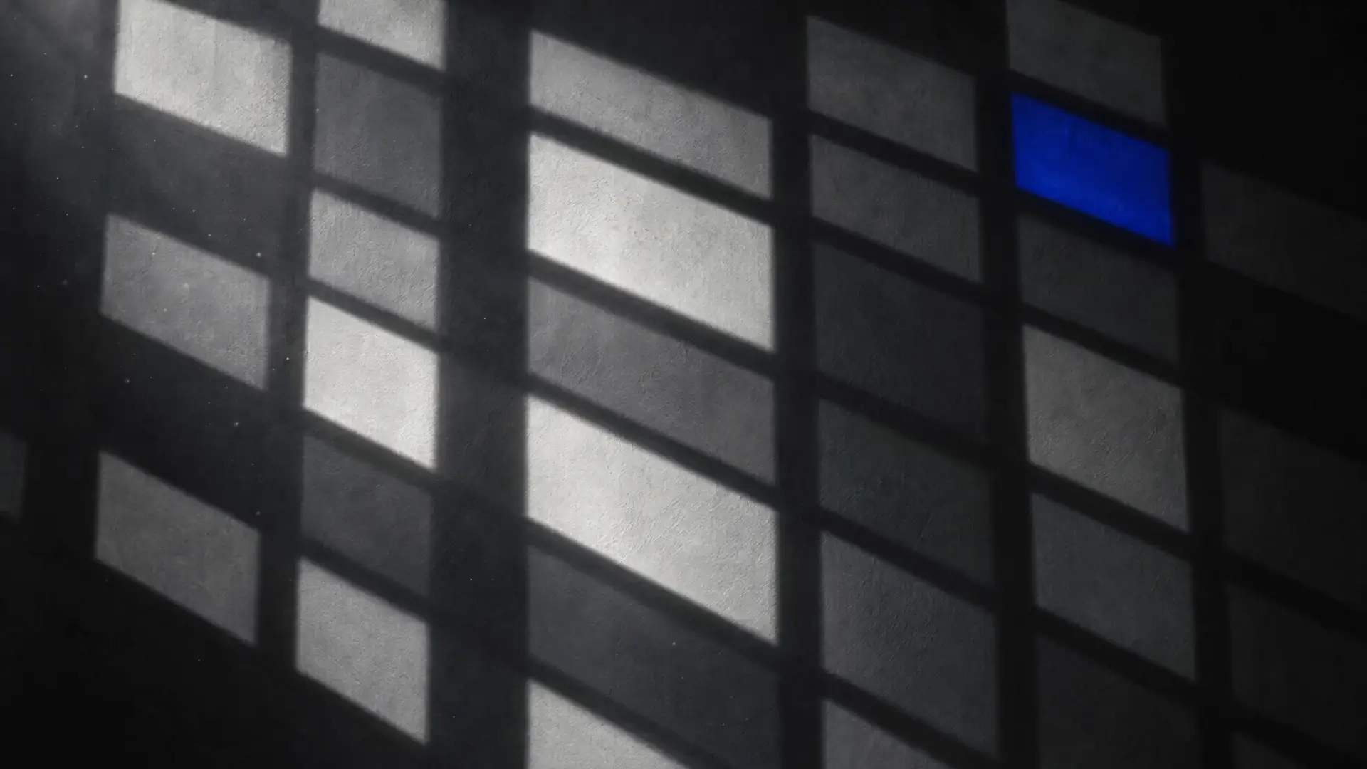 A grid of pale light and a single Klein blue pane cast through monochrome stained glass onto a dark wall